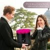 Mann der einer Frau eine schwarze runde Rosenbox mit lila pinken Infinityrosen überreicht
