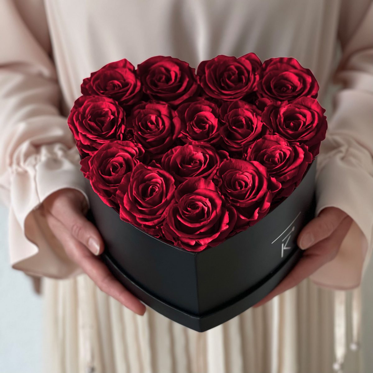 Herzförmige Rosenbox mit roten Infinityrosen wird in den Händen gehalten