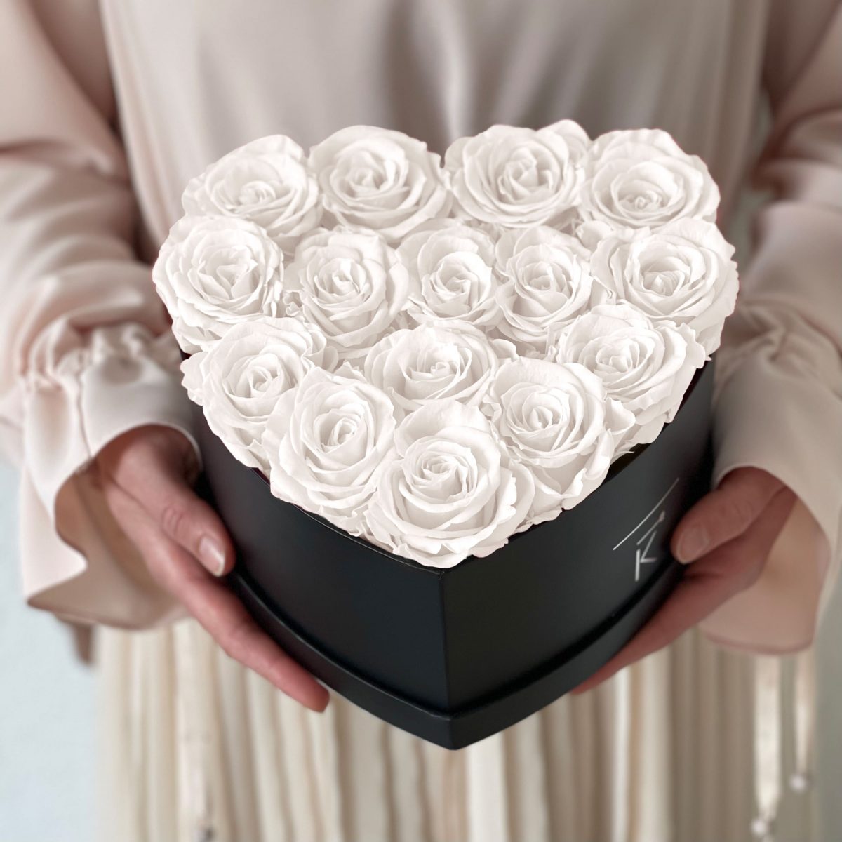 Herzförmige Rosenbox mit weißen Infinityrosen wird in den Händen gehalten