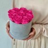 Runde Rosenbox aus hellgrauem Samt mit lila pinken Infinityrosen wird in den Händen gehalten