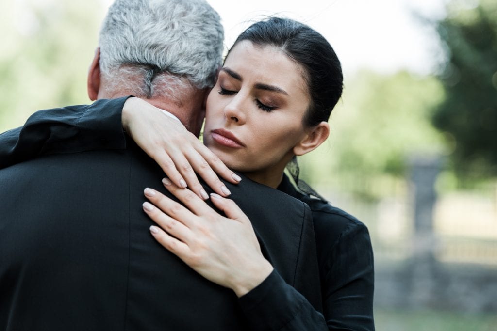 Schwarz gekleideter Mann umarmt eine Frau bei einer Beerdigung
