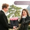Mann der einer Frau eine schwarze runde Rosenbox mit rosanen Infinityrosen überreicht