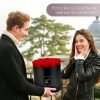 Mann der einer Frau eine schwarze runde Rosenbox mit roten Infinityrosen überreicht